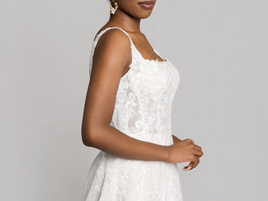 Close-up side view of a bride in a lace wedding dress with thin straps, wearing statement earrings and an updo hairstyle.