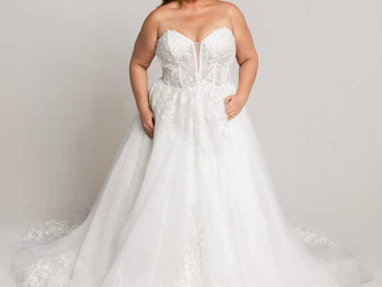 Bride wearing a strapless lace wedding gown with a sweetheart neckline and full tulle skirt, standing against a neutral background.