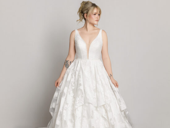 Bride in a sleeveless lace wedding dress with a full skirt, standing against a neutral background.