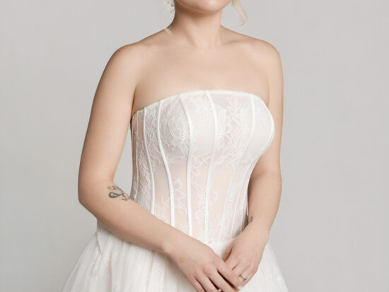 Close-up of a bride wearing a strapless lace corset-style wedding gown with a structured bodice and full tulle skirt.