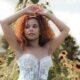Bride in a lace wedding dress stands in a sunflower field with arms raised, surrounded by tall sunflowers in warm sunlight.