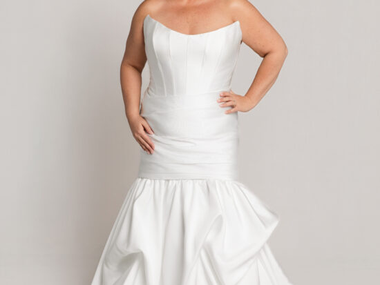 Bride wearing a strapless white wedding gown with a fitted bodice and mermaid-style skirt with ruffled detailing, posing against a neutral background.