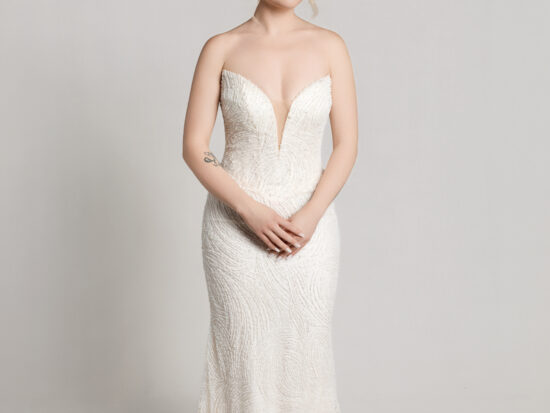 Bride wearing a strapless white wedding gown with a flowing full skirt, holding the sides of the dress while standing against a neutral background.