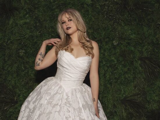 Bride in a floral textured ball gown standing in front of a green foliage wall with a chapel train spread behind her.