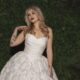 Bride in a floral textured ball gown standing in front of a green foliage wall with a chapel train spread behind her.