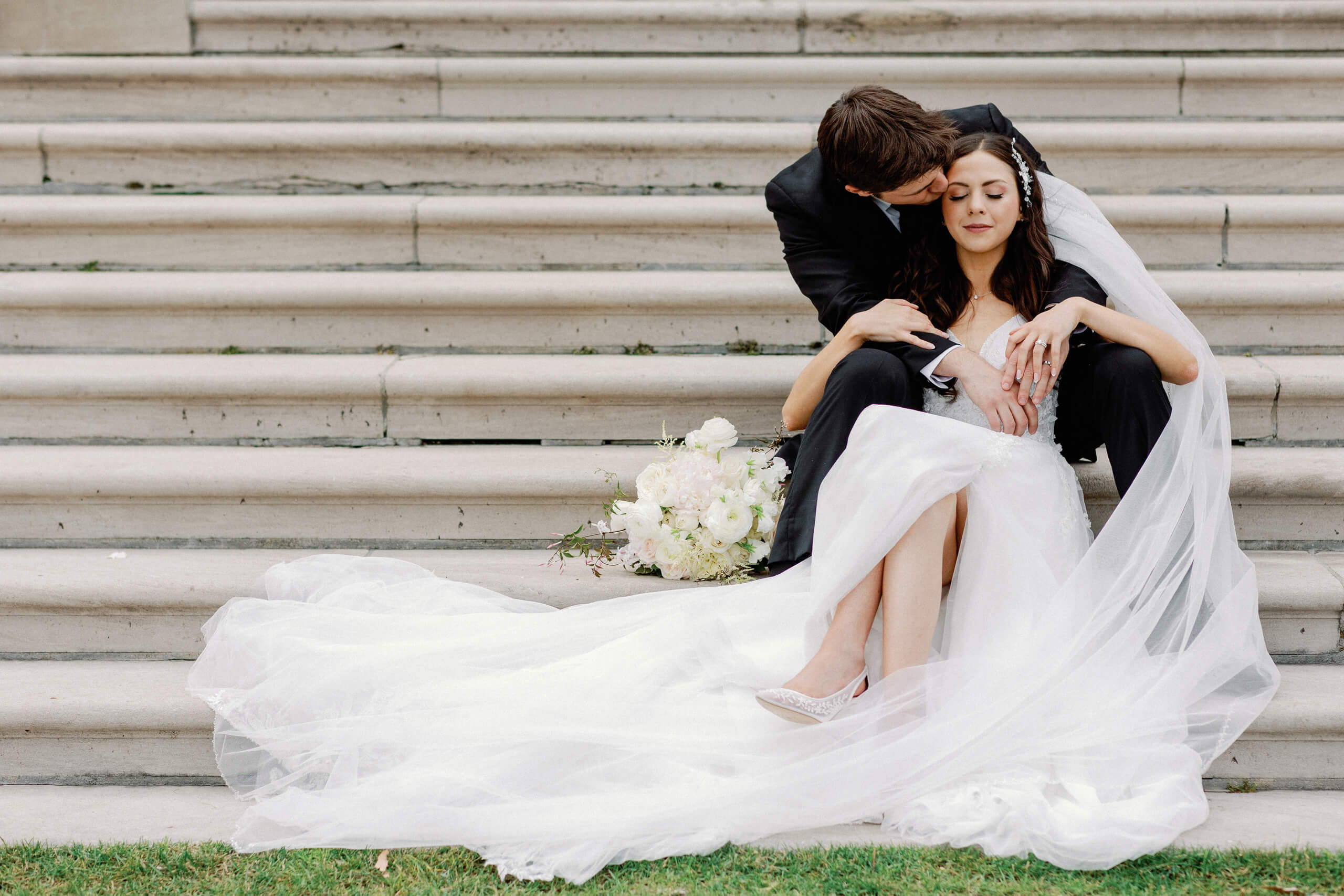 Bride seated between the legs of the groom with her dress spread out with her legs.