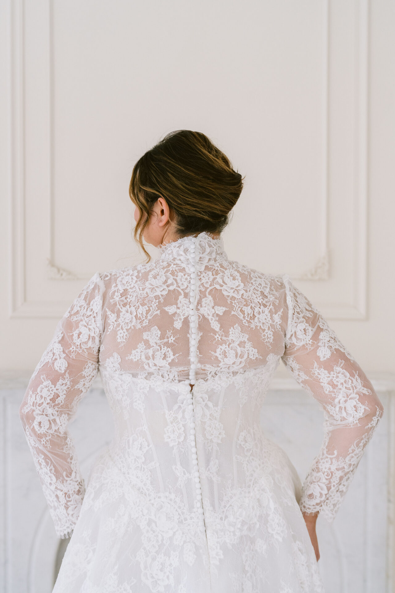 Close-up back detail of a curve lace wedding dress with sheer long sleeves and button closure.