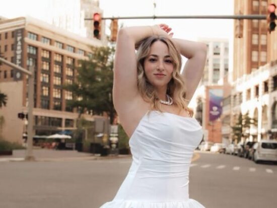 Bride in a strapless white wedding gown posing in the middle of a city street with buildings and traffic lights in the background.