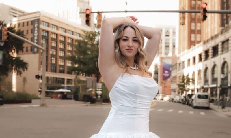 Bride in a strapless white wedding gown posing in the middle of a city street with buildings and traffic lights in the background.