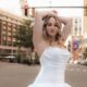 Bride in a strapless white wedding gown posing in the middle of a city street with buildings and traffic lights in the background.