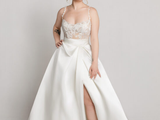 Bride wearing a sleeveless wedding gown with a fitted bodice and full skirt with a high slit, posing against a neutral background.