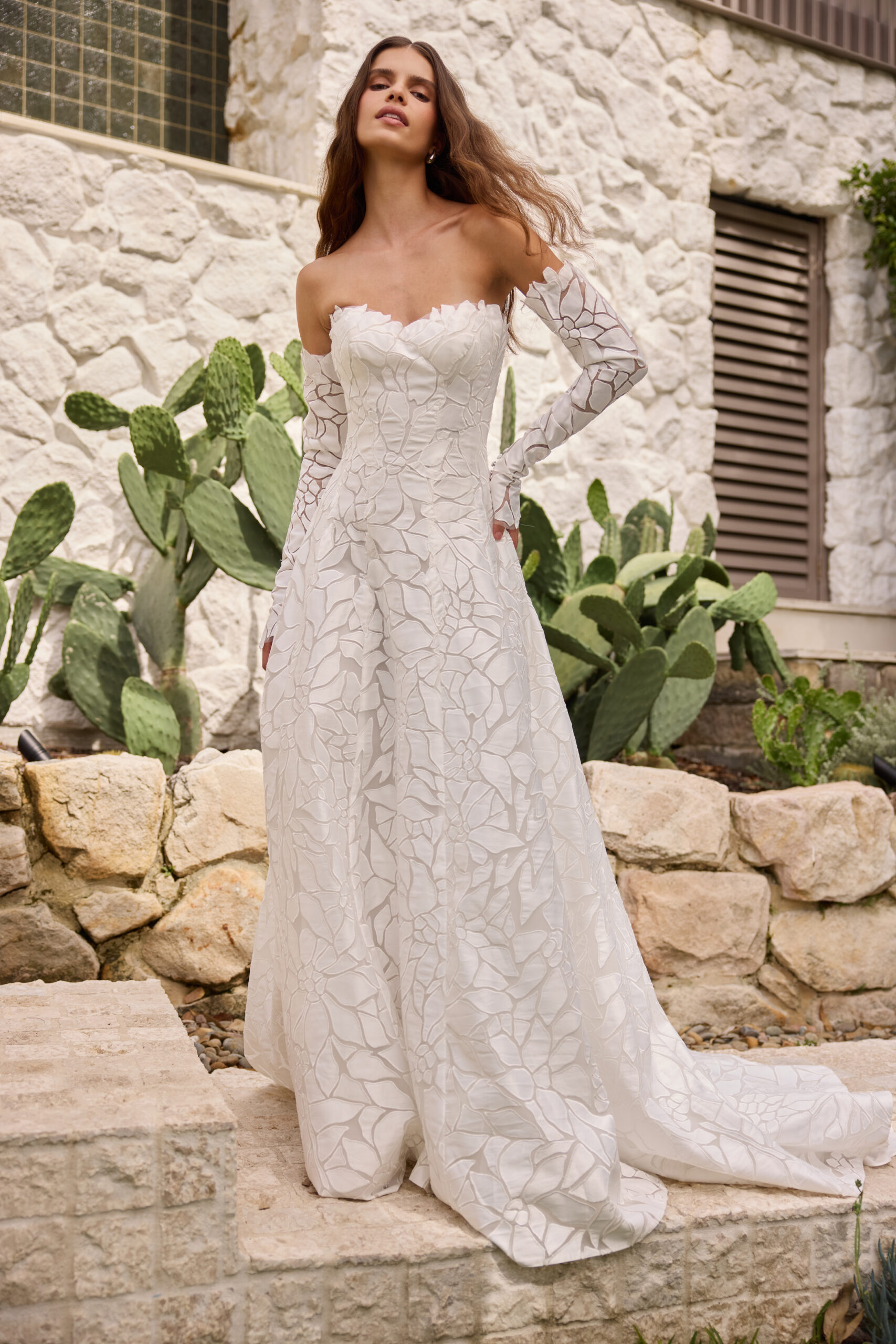 Bride in a strapless gown standing on stone steps in a natural setting.