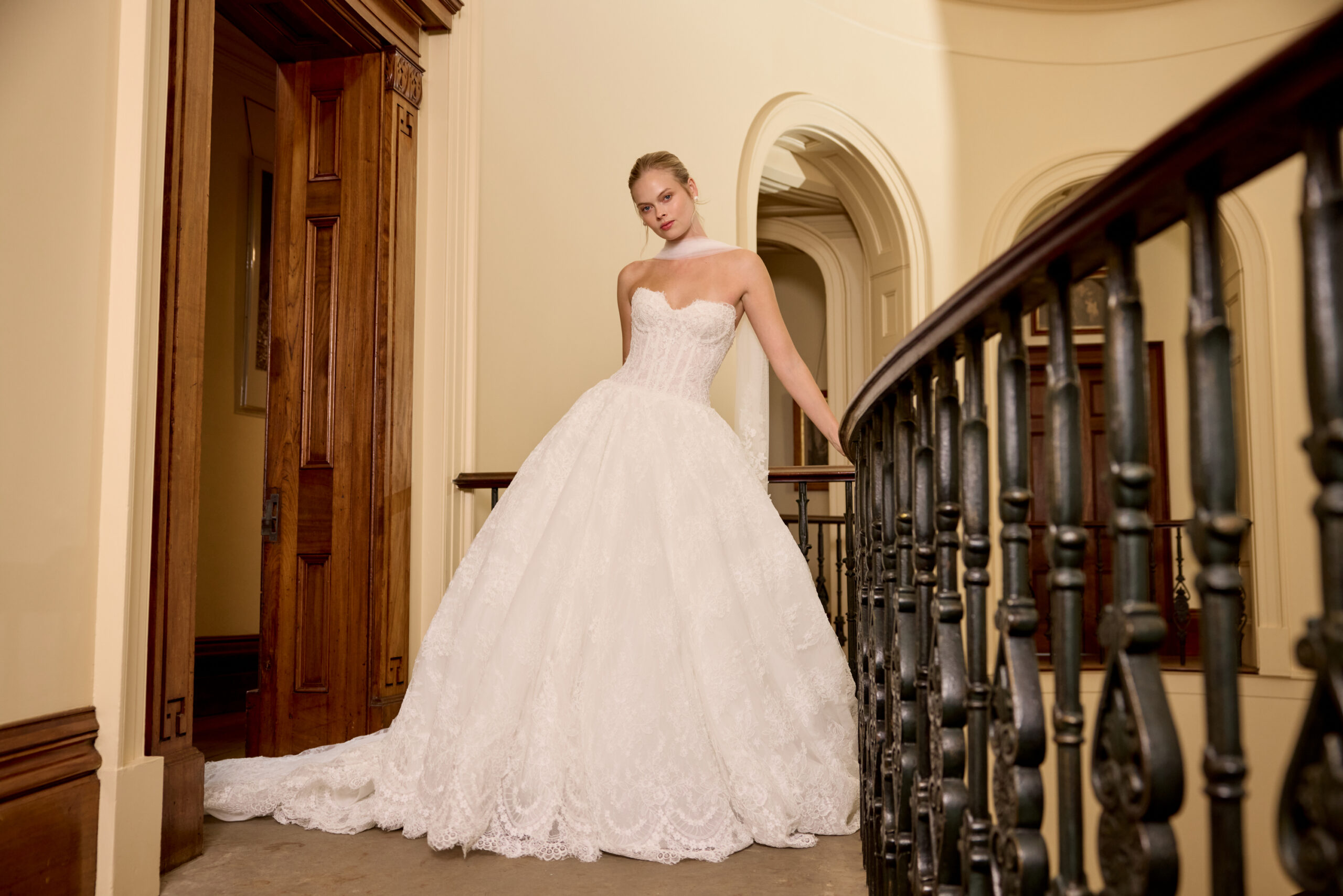 Bride wearing a strapless ball gown posing along an ornate indoor balcony railing.