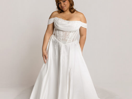 Bride wearing an off-the-shoulder white wedding gown with a full flowing skirt, standing against a neutral background.