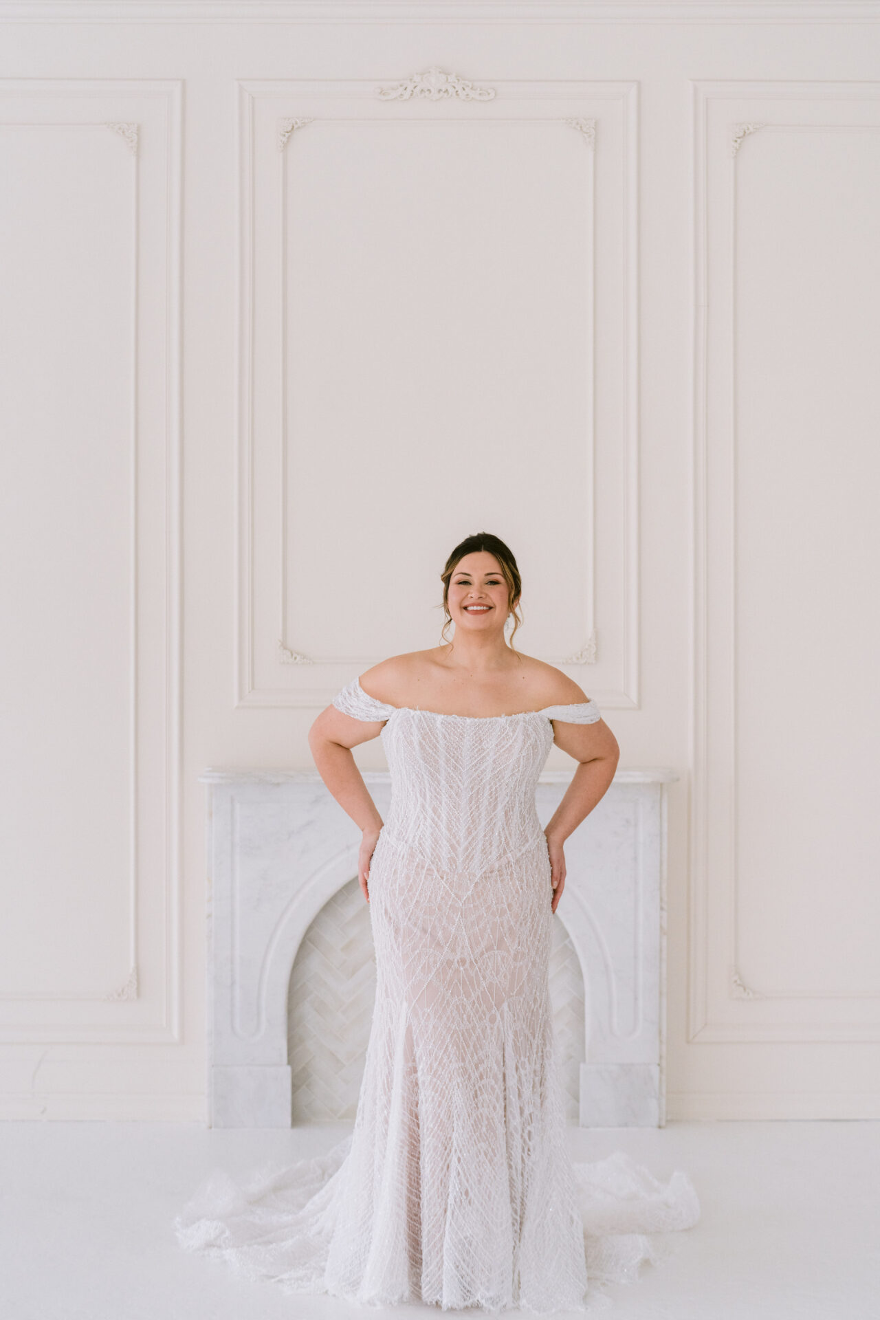 Front view of a bride in a plus size off-shoulder fitted wedding dress with elegant silhouette.