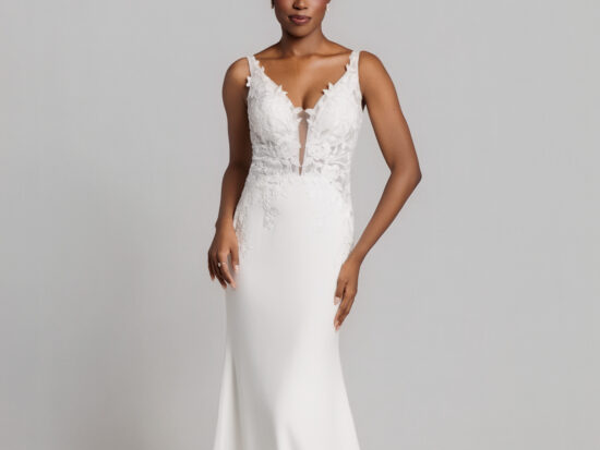 Bride wearing a sleeveless white wedding gown with a deep V-neckline and fitted silhouette, standing against a neutral background.