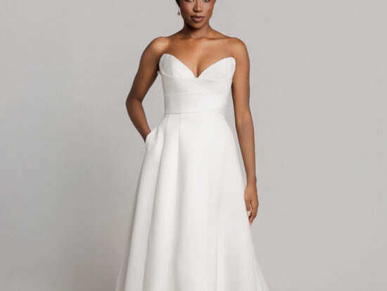 Bride wearing a strapless white wedding gown with a sweetheart neckline and A-line skirt, posing against a neutral background.