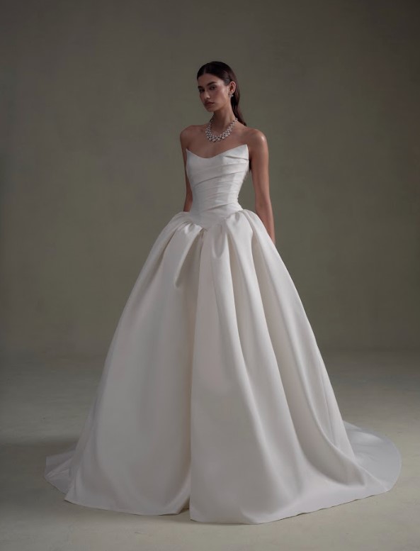 Bride wearing a strapless white ball gown with a structured bodice and full skirt, posing against a neutral studio backdrop.
