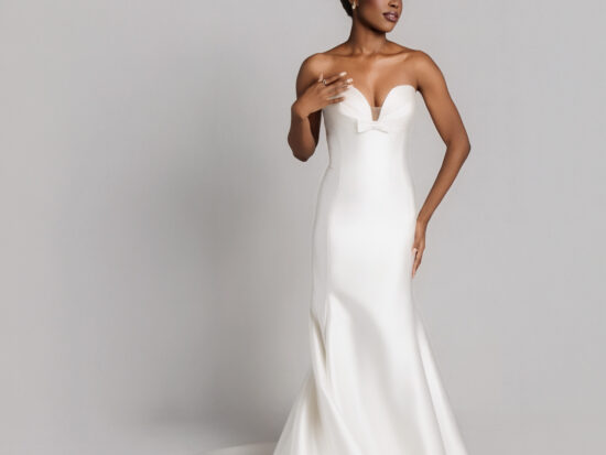 Bride wearing a strapless fitted white wedding gown with a sweetheart neckline and long train, posing against a neutral background.