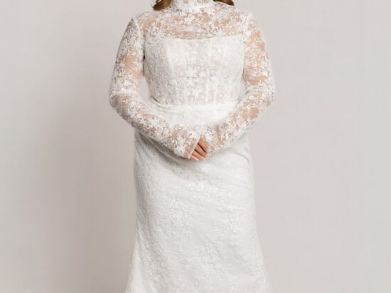 Bride wearing a high-neck long-sleeve lace wedding gown with a fitted silhouette, standing with hands clasped against a neutral background.