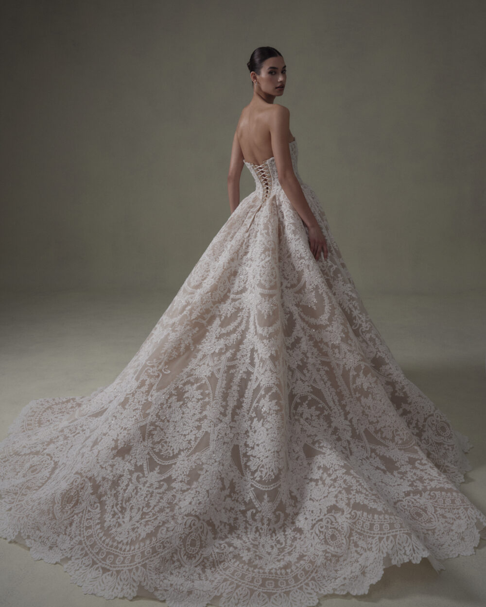 Model shown from the back in a lace ball gown wedding dress with a corset bodice and cathedral-length train.