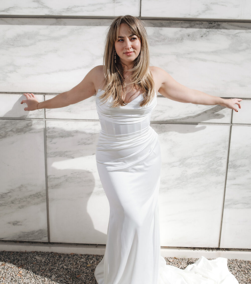 woman in bridal dress with her arms wide open and standing against a wall