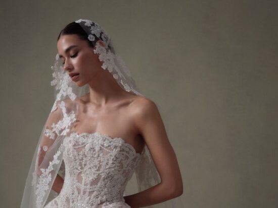 Close-up portrait of a model in a lace strapless wedding gown wearing a floral-edged veil.