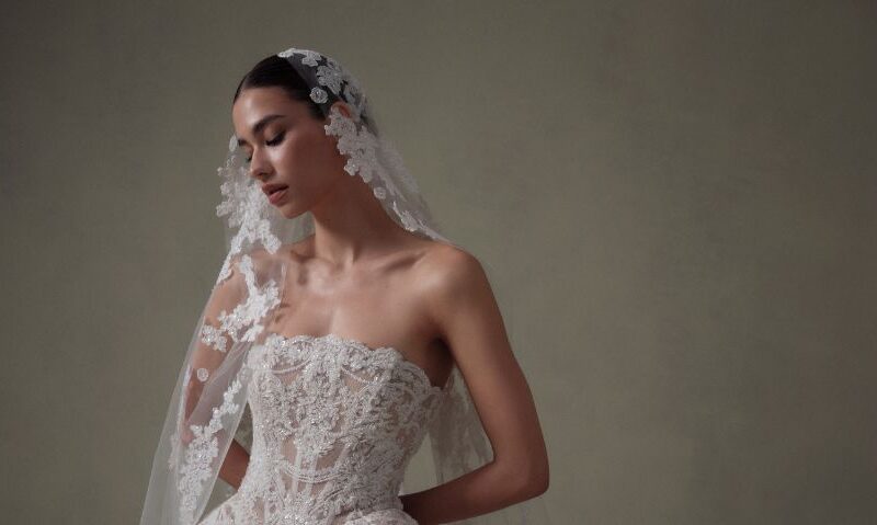 Close-up portrait of a model in a lace strapless wedding gown wearing a floral-edged veil.