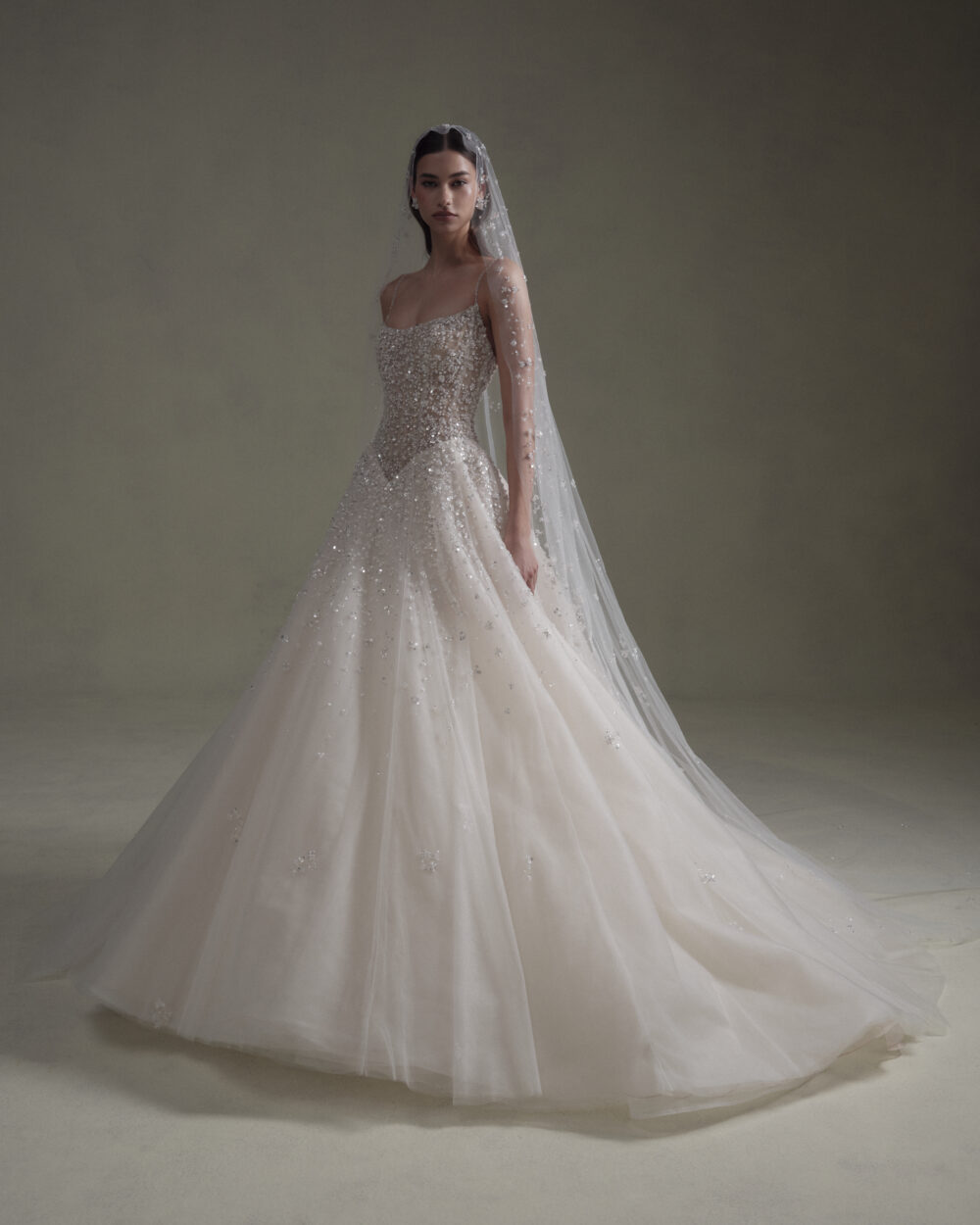Model wearing a sparkling sleeveless ball gown wedding dress with an embellished veil posed in a studio.