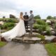 Outdoor wedding ceremony with the bride and groom exchanging vows on a stone platform, surrounded by bridesmaids and groomsmen.