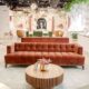 Spacious bridal boutique showroom with velvet seating, floral wall murals, chandeliers, and wedding gowns displayed along large windows.