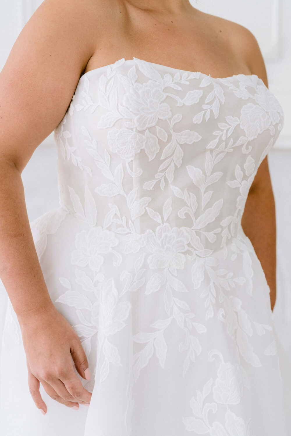 A close-up view of a strapless wedding gown featuring floral lace appliqué and sheer fabric detailing on the bodice.