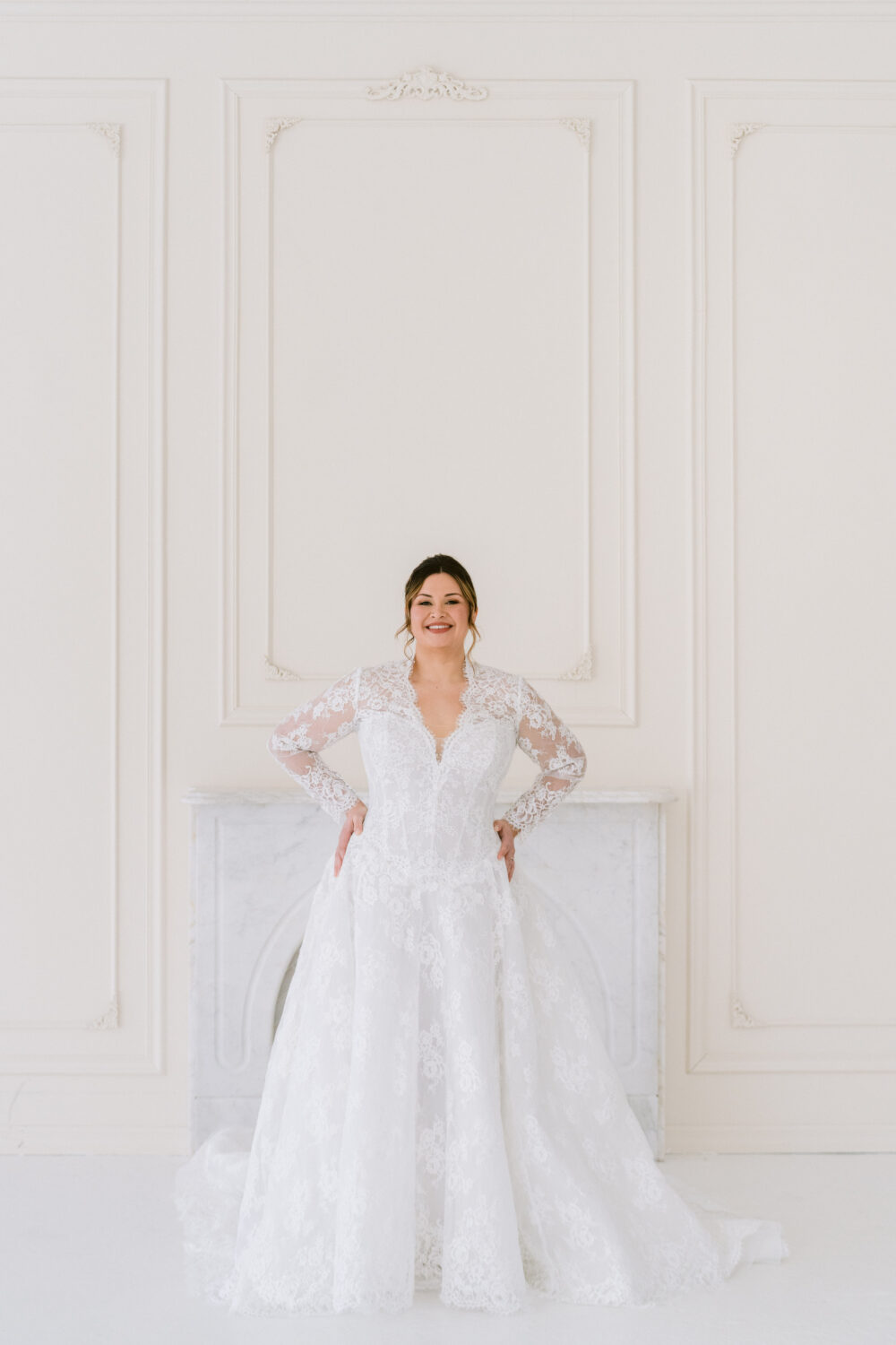 A bride models a fitted off-the-shoulder wedding dress with sheer long sleeves in a white studio with overlaid promotional text.