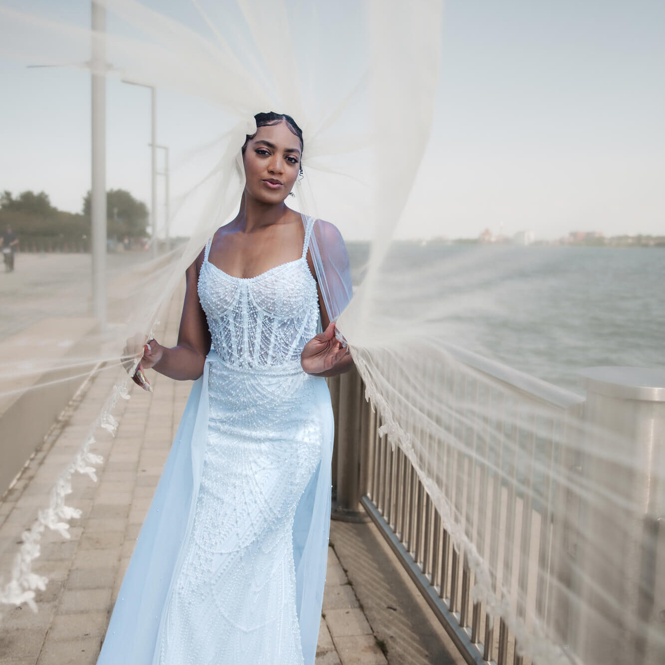 Bride standing outdoors on a bridge wearing a blue flowing wedding gown with a long train blowing in the wind.