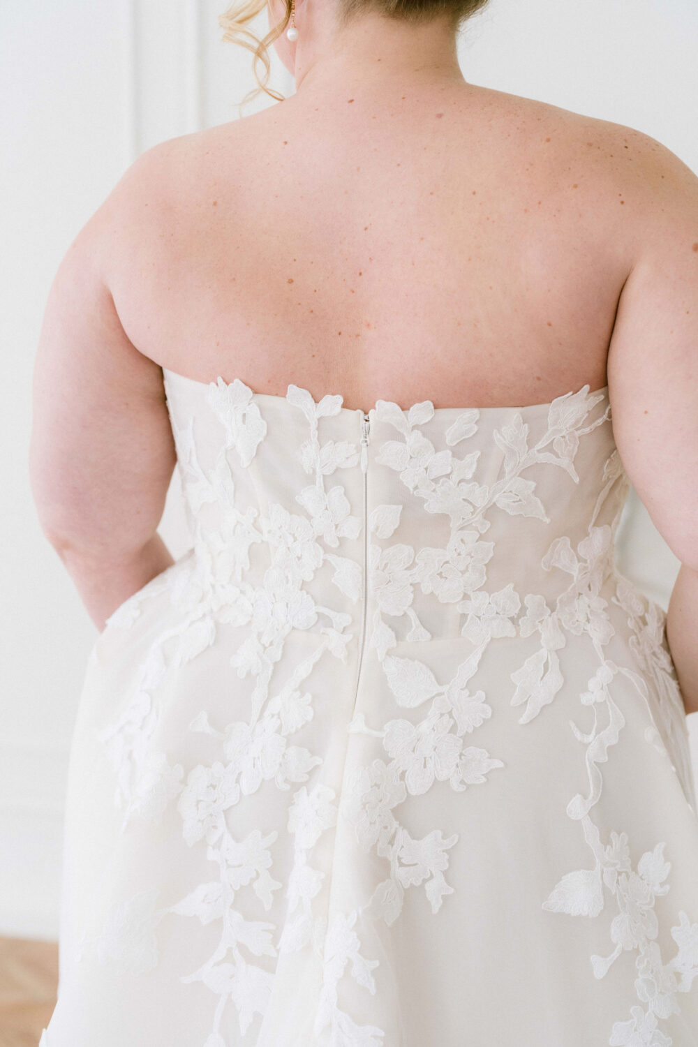 A close-up view of the back of a strapless wedding gown with floral appliqué detailing and a center zipper closure.