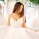 Bride in a sparkling tulle ball gown with a lace bodice stands in a bridal boutique beneath hanging crystal chandeliers and greenery.