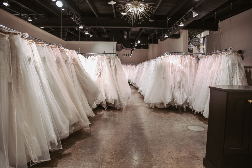 Spacious bridal boutique with long rows of wedding dresses displayed on garment racks beneath modern lighting.