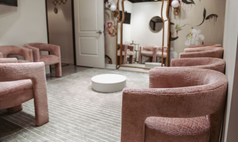 Cozy bridal fitting lounge with plush pink chairs, full-length mirrors, and a round white coffee table.
