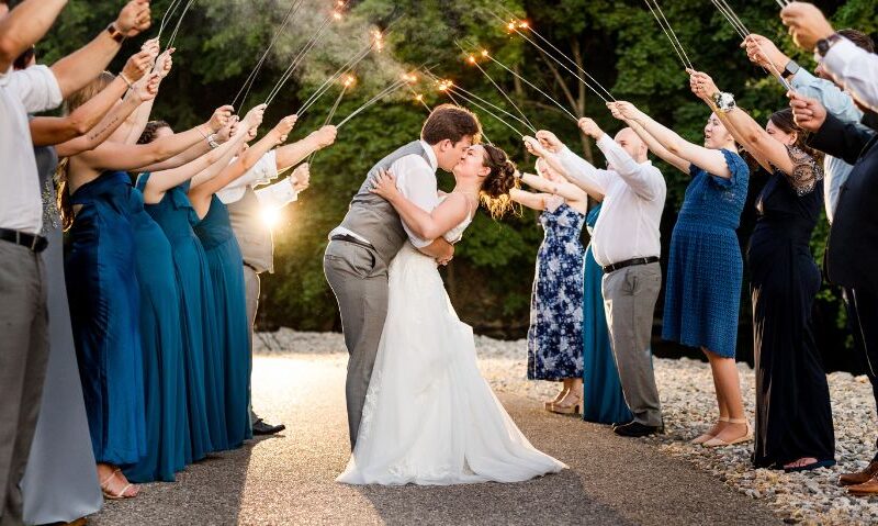 Bride and groom kiss during a sparkler exit as wedding guests line both sides of the walkway holding sparklers.
