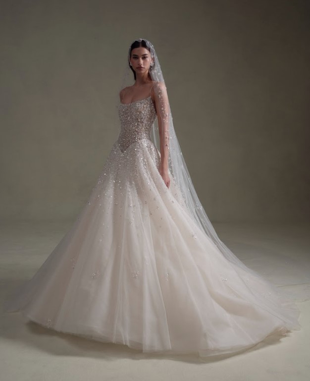 Bride wearing a sparkling ball gown with a fitted bodice and flowing tulle skirt against a neutral studio backdrop.