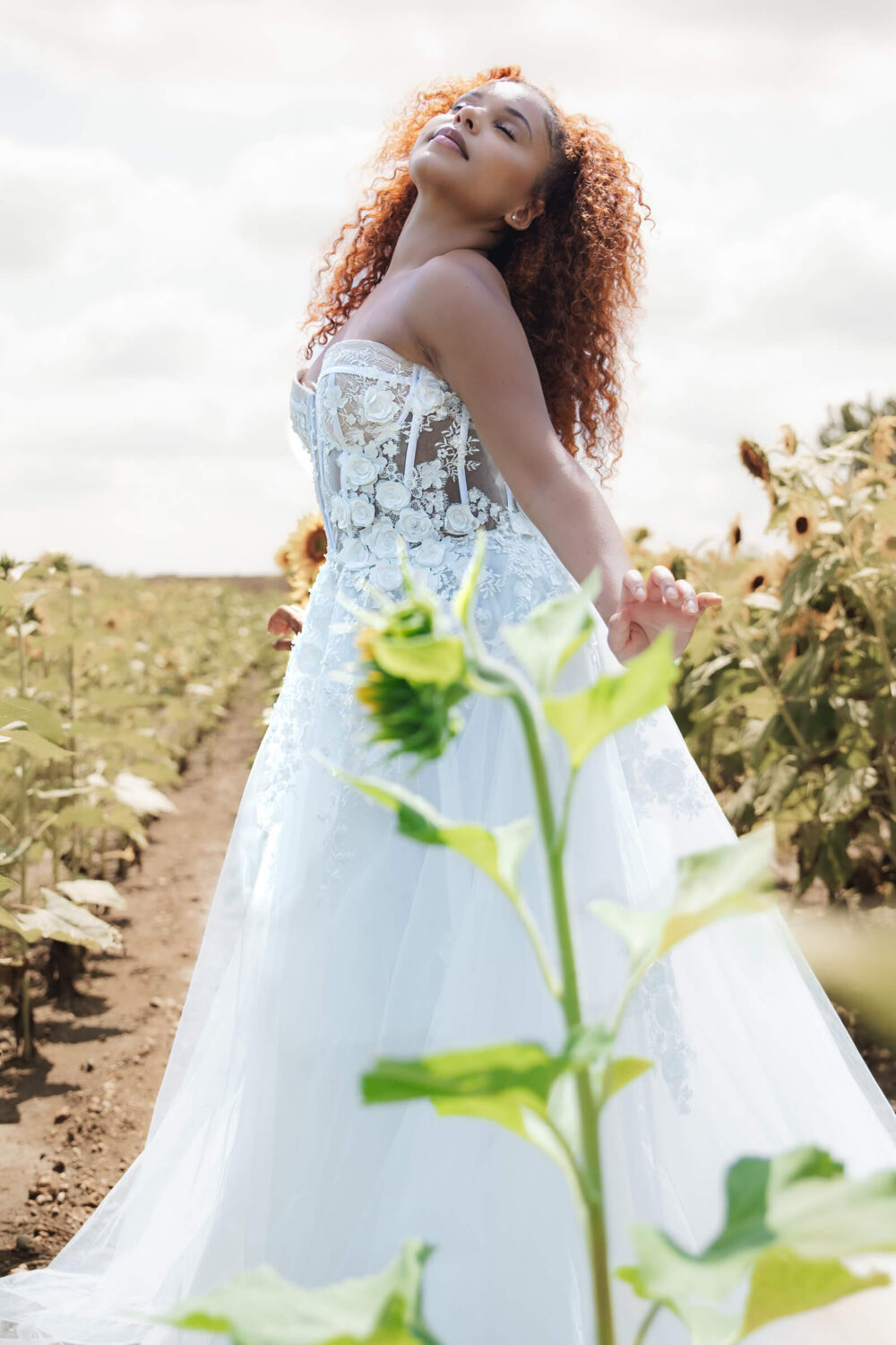 Bride in a floral embroidered wedding dress posing in a sunlit flower field.
