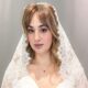 Close-up portrait of a bride wearing a lace-edged veil over a satin wedding dress against a gray backdrop.