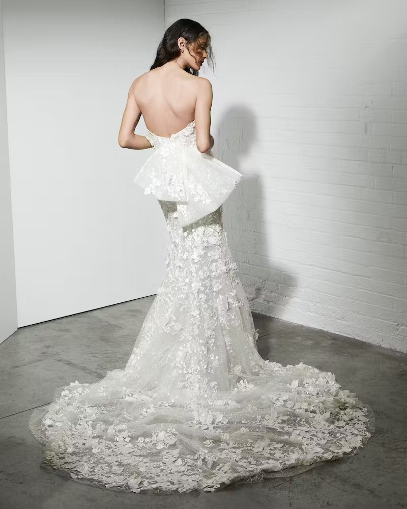 Back view of a bride wearing a modern mermaid wedding gown with a sculptural peplum and textured floral train.