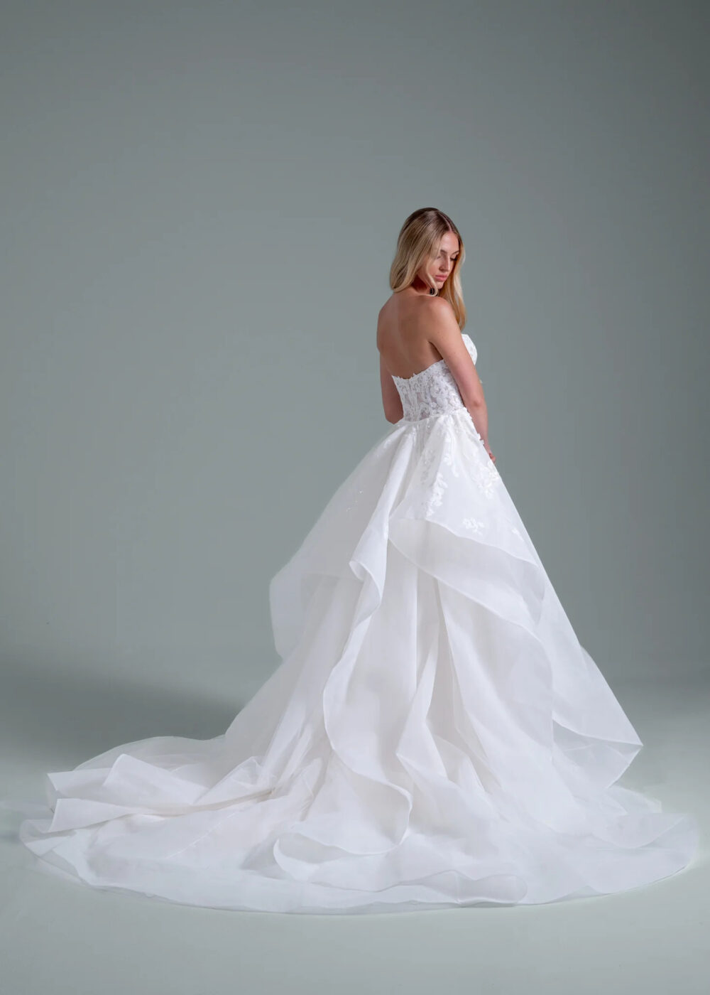 Bride wearing a simple strapless wedding gown with a dramatic layered skirt in a minimalist studio.
