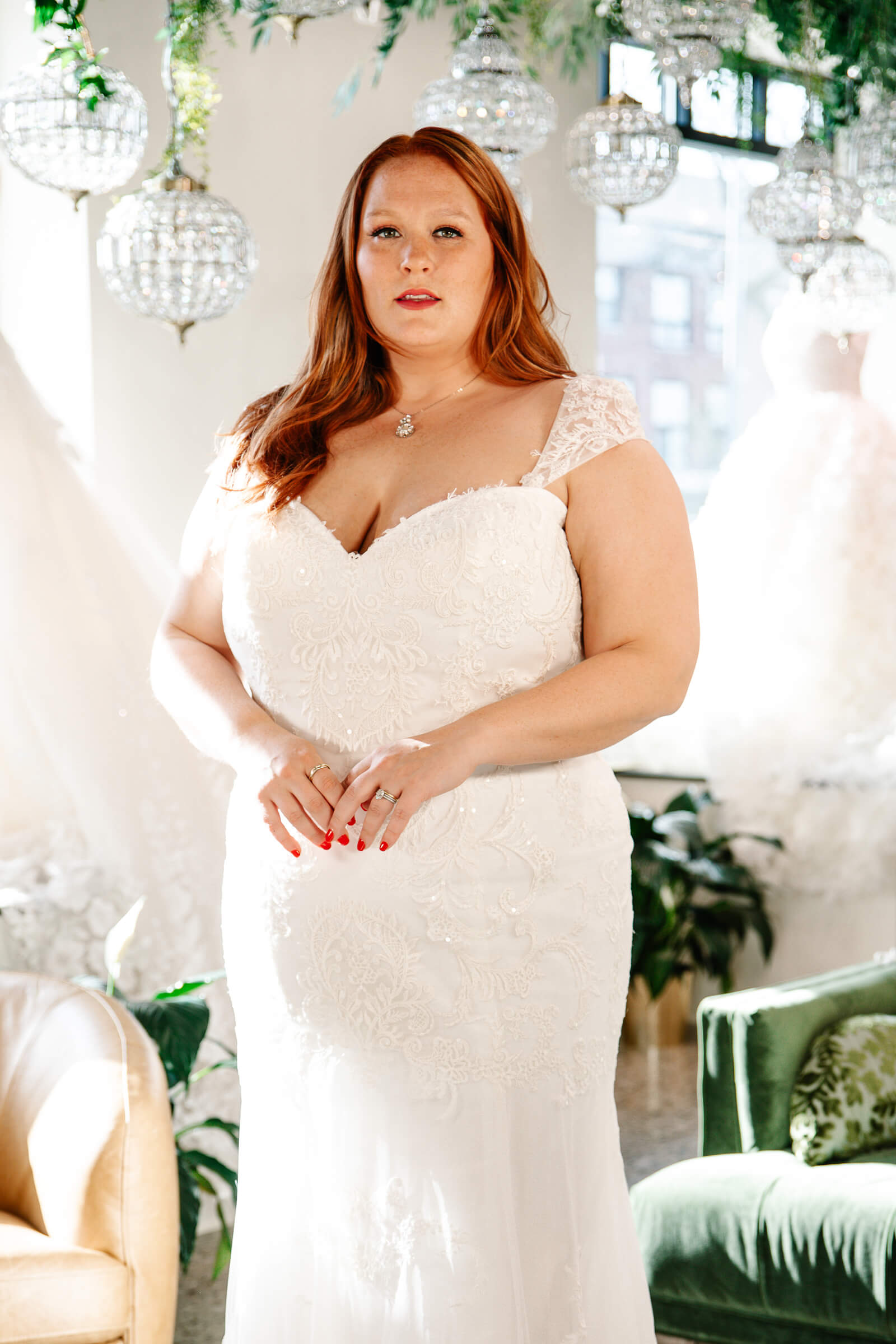 Bride wearing a fitted lace wedding gown with cap sleeves inside a bright bridal boutique.