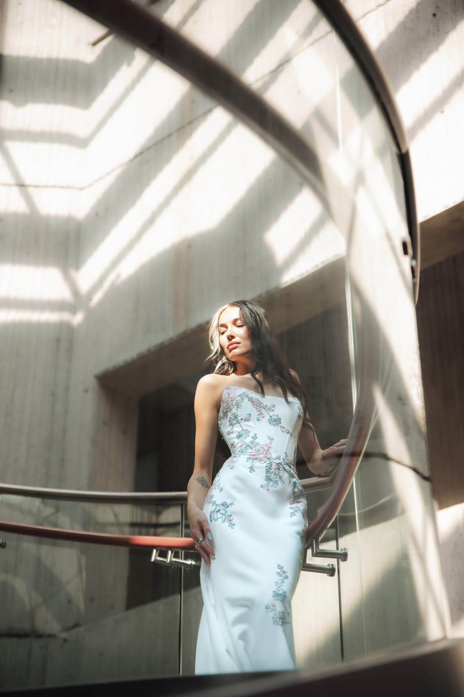Bride wearing a sleek floral wedding gown while standing in a modern building filled with natural light.