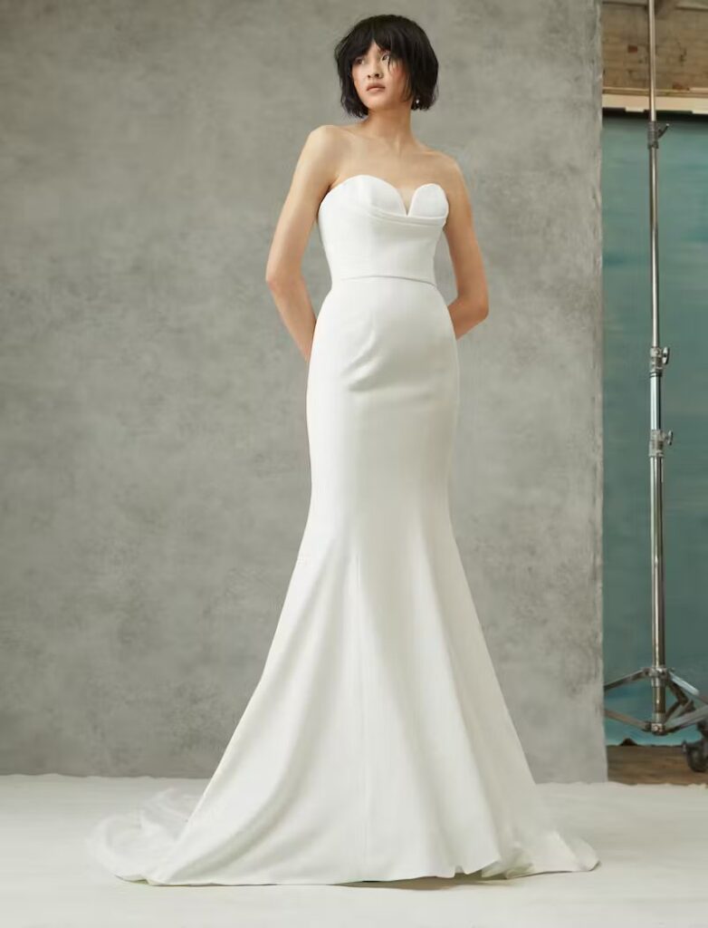 Bride wearing a sleeveless sweetheart mermaid wedding dress against a neutral studio backdrop.