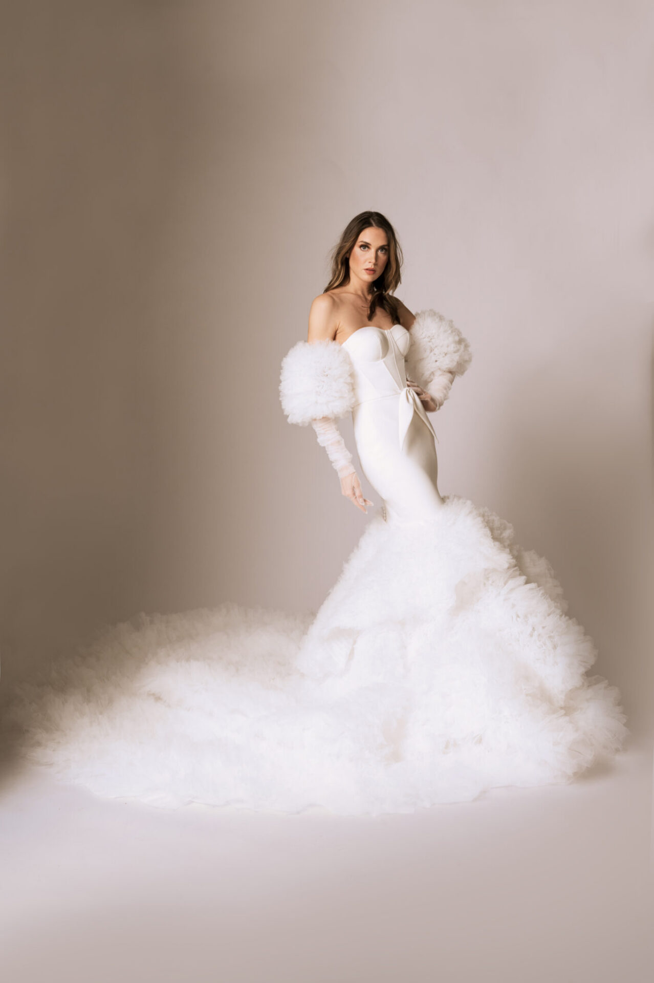 Bride wearing a modern wedding gown with oversized puff sleeves and a dramatic ruffled skirt against a neutral backdrop.