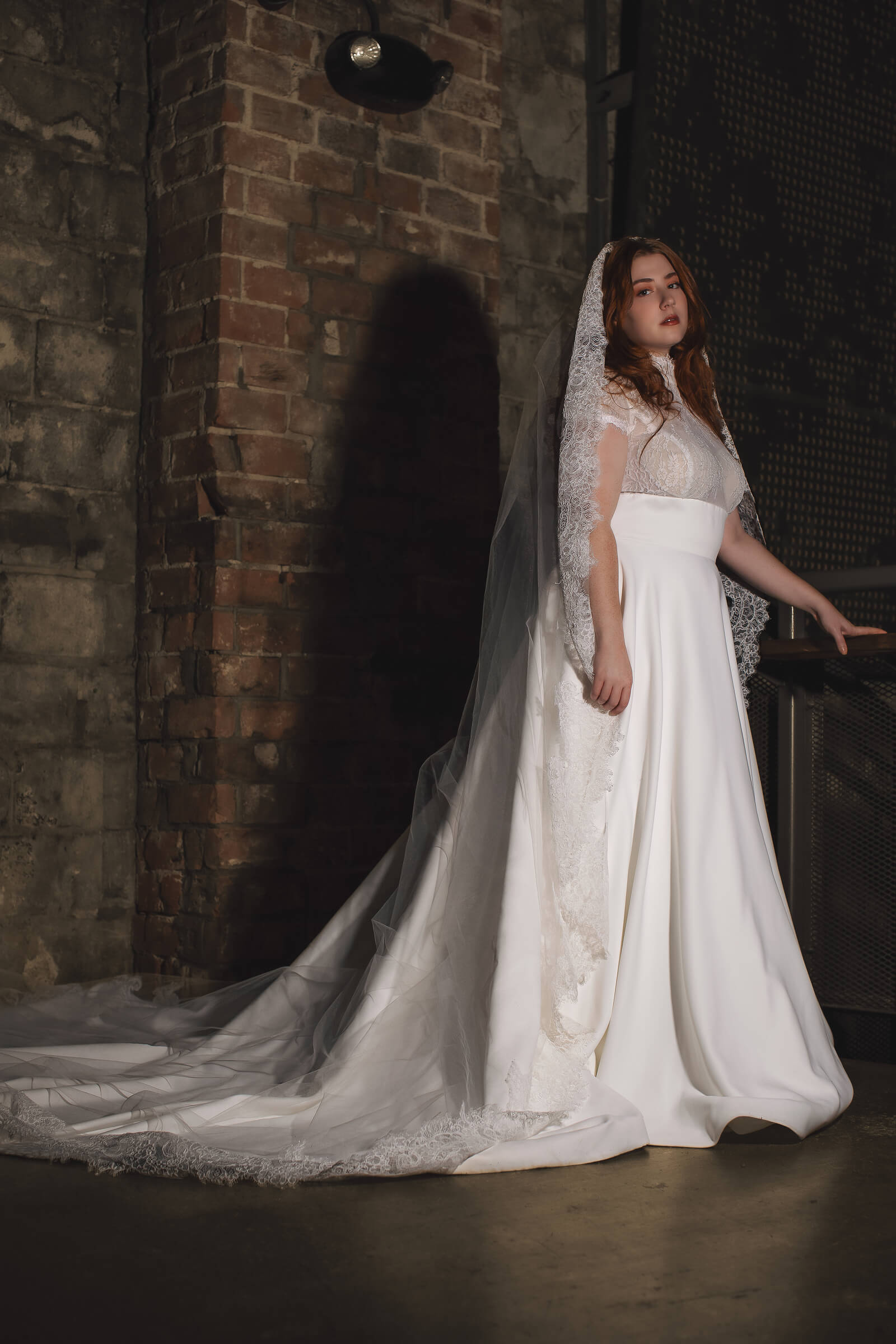 A bride in a white wedding gown poses in a rustic setting, showcasing her bridal hairstyle and accessories.