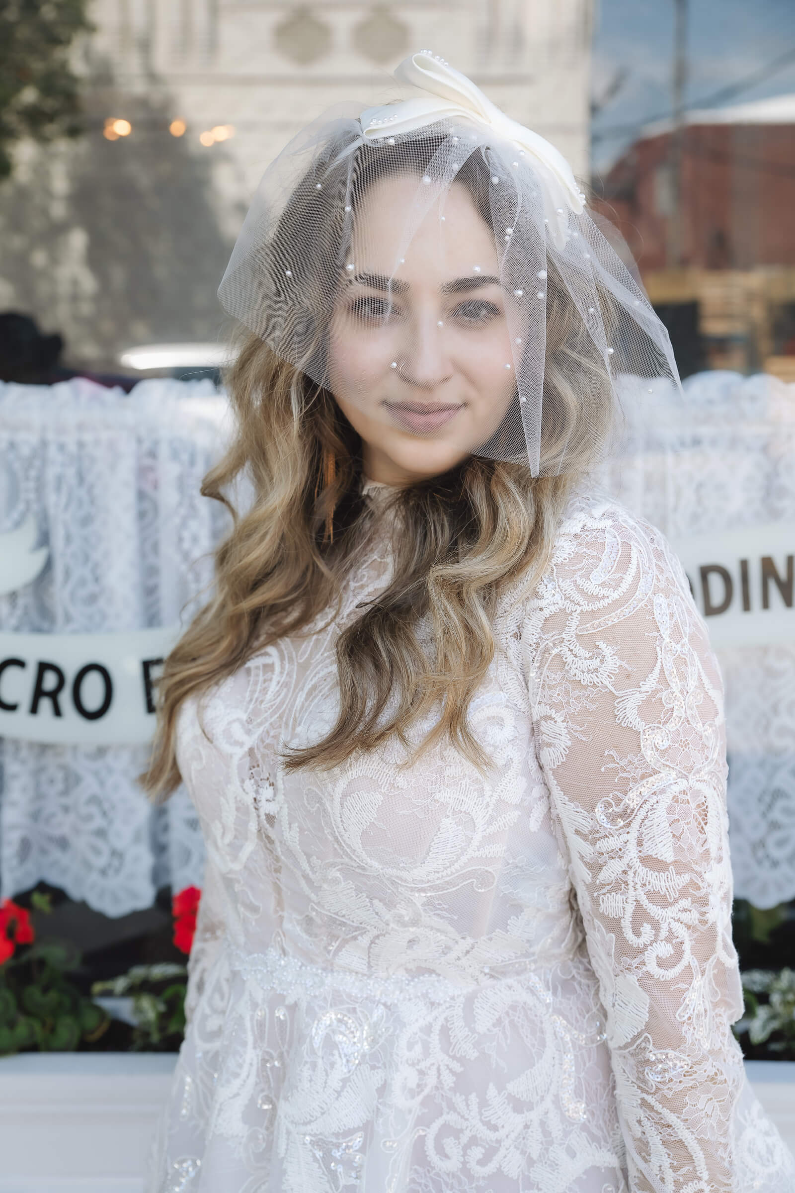 A bride with long wavy hair and a lace wedding gown poses outdoors, showcasing her bridal hairstyle.